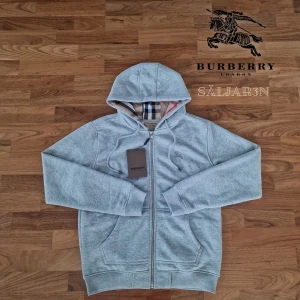 Burberry Hoodie  - Letar du efter en stilren och lyxig hoodie? Denna helt nya grå Burberry-hoodie kombinerar elegans med hög komfort. Den har Burberrys ikoniska rutmönster i fodret och en diskret logga på bröstet för en exklusiv touch. Tillverkad av mjukt, slitstarkt material och utrustad med dragkedja samt huva – både praktisk och stilfull.  📌 Skick: Ny med taggar. 📦 Snabb leverans – skickas samma dag! .