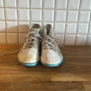 Nike Mercurial Superfly 9  - Snygga Nike Mercurial fotbollsskor i vitt med ljusblå och svarta detaljer. Skorna har snörning, högre skaft och mönstrad sula med dobbar för gräsplan. Stora Nike-loggor på sidorna och Mercurial-tryck baktill. Perfekta för dig som vill sticka ut på planen.                                                   Obs!!! Saknar sula