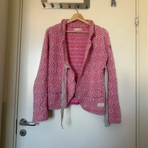 Rosa och vit mönstrad kofta Odd Molly - Säljer en mysig kofta från Odd Molly i rosa och vitt med snyggt mönster över hela plagget. Koftan har långa ärmar, knytband framtill och en broderad logga på ärmen. Materialet är stickad bomull, perfekt för att ge din outfit lite färg och stil. Storlek 2 som enligt deras storleksguide motsvarar en storlek M. Fint skick, men kan vara något mer använd. Se bild 2 för anmärkning. 