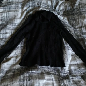 Svart ribbad polotröja från Zara - Svart polotröja från Zara med ribbad struktur och lång ärm. Tröjan har en klassisk polokrage och är gjord i mjukt material som sitter skönt mot kroppen. Perfekt för lager-på-lager och enkel att matcha med jeans eller kjol.