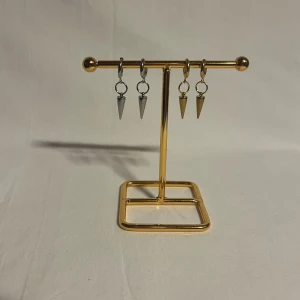 Örhängen med spetsiga hängen i silver och guld - Säljer två par örhängen med coola spetsiga hängen, ett par i silverfärg och ett par i guldfärg. Båda har en minimalistisk design med små ringar och konformade hängen som ger en edgy vibe. Perfekt för dig som gillar att sticka ut med detaljer.