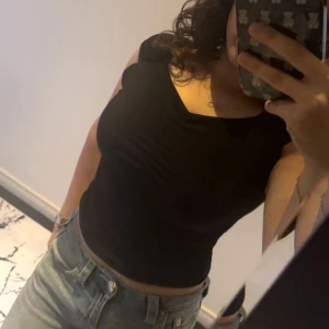 Svart ruched topp från Barrel and Oil - Säljer en svart topp från Barrel and Oil med snygg rynkad detalj framtill och lätt puffade axlar. Toppen är croppad och har en v-ringad halsringning. Perfekt att styla med jeans eller kjol för en trendig look.