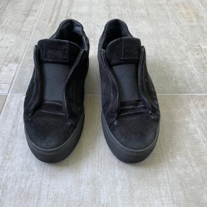 Svarta Axel Arigato clean 360 laceless - Säljer ett par svarta sneakers från Axel Arigato i mocka med stilren design och platt sula. Skorna har elastisk panel över vristen istället för klassisk snörning, vilket ger en clean look. Perfekta för dig som gillar minimalistisk stil och vill ha något som sticker ut.