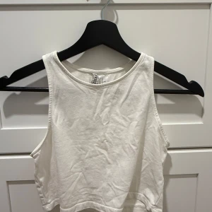 Vit croppad linnetopp från H&M Divided - Säljer en enkel och fräsch vit croppad linnetopp från H&M Divided. Toppen är ärmlös med rund halsringning och tillverkad i mjuk bomull. Perfekt att matcha med jeans eller kjol för en clean look.