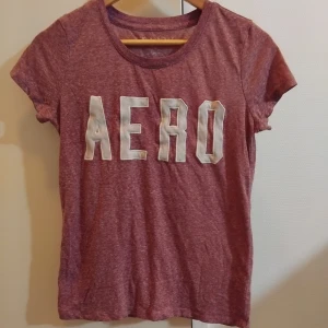 Vinröd t-shirt från Aeropostale - Snygg vinröd t-shirt från Aeropostale med stort vitt AERO-tryck på bröstet. T-shirten är kortärmad och har en klassisk rund halsringning. Materialet är mjukt och skönt, perfekt för en avslappnad stil. Den är jätteliten så S/M I äntligen:)