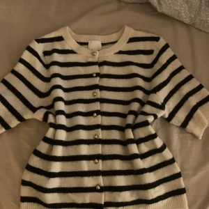 Randig kofta från H&M i svart och vitt - Supermysig kofta från H&M i svart och vitt med klassiskt randigt mönster. Koftan har rund halsringning, knappar framtill och trekvartsärmar. Perfekt att slänga på sig över en t-shirt eller linne för en chill look.