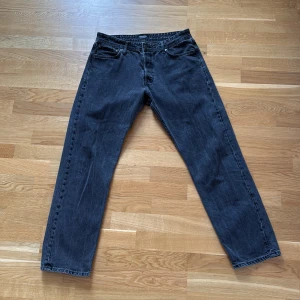 Svarta jeans från Jack & Jones - Säljer ett par svarta jeans från Jack & Jones med klassisk femficksdesign och raka ben. Jeansen har en mörk tvätt och subtila slitningar för en cool look. Passar dig som gillar enkel stil med lite edge. Perfekt till sneakers eller boots.