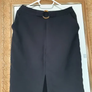 Svart pennkjol från Mint & Berry - Stilren svart pennkjol från Mint & Berry i storlek 38. Kjolen har en snygg slits framtill, fickor i sidorna och ett dekorativt bälte i midjan.