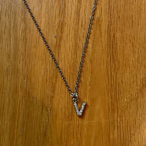 Halsband med glittrigt V-hänge - Snyggt halsband i silverfärgad kedja med ett glittrande V-format hänge täckt av små stenar. Perfekt accessoar för dig som vill ha något personligt och stilrent. Kedjan är tunn och smidig, passar till många olika looks. Priset kan diskuteras💕