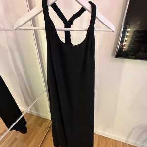 Svart långklänning från Monki XS - Svart långklänning från Monki i storlek XS. Klänningen har flätade axelband som korsas i ryggen och en rak, flowy passform. Perfekt för dig som gillar minimalistisk stil och vill ha något bekvämt men ändå snyggt.