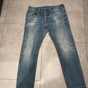 Blå jeans från G-Star RAW - Snygga blå jeans från G-Star RAW med klassisk femficksdesign och slitna detaljer för en cool, avslappnad look. Jeansen har normal passform och raka ben, med läderpatch bak i midjan och diskreta sömmar på bakfickorna. Perfekta till sneakers eller boots.