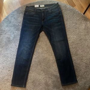 Mörkblå jeans från Stock & Hank - Snygga mörkblå jeans från Stock & Hank med klassisk femficksdesign och raka ben. Jeansen har dragkedja och knapp i midjan samt diskreta slitningar för en modern look. Perfekta till vardags och passar till det mesta. Strl 31/30.