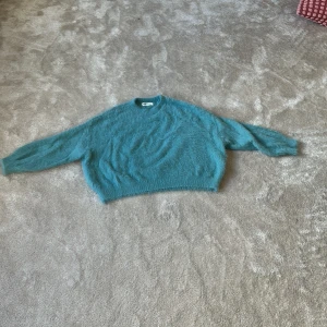 Turkos fluffig tröja från H&M - Mysig turkos fluffig tröja från H&M med rund halsringning och lång ärm. Perfekt för kyligare dagar och ger en trendig look med sin oversized passform och mjuka material.