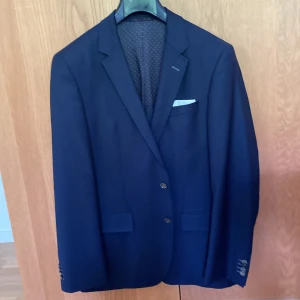 Mörkblå kavaj från Bertoni - Snygg mörkblå kavaj från Boss med klassisk passform. Kavajen har två knappar framtill, fyra dekorativa knappar vid ärmslut och ett vitt näsduk i bröstfickan. Perfekt för bal eller fest.