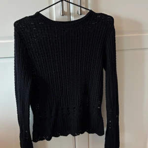 Svart stickad tröja från Tezenis - Säljer en svart stickad tröja från Tezenis med lång ärm och rund halsringning. Tröjan har ett genombrutet mönster och vågig kant nertill, vilket ger en snygg och trendig look. Perfekt att styla med jeans eller kjol.