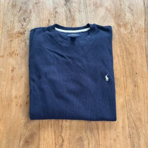 Polo Ralph Lauren – Mörkblå långärmad tröja i bomullsblandning - Mjuk och stilren långärmad tröja i mörkblå waffle-stickad bomullsblandning, med klassisk vit broderad logga på bröstet. Perfekt som loungewear eller vardagsplagg.  Storlek: XL (liten i storleken, passar M - L)  Färg: Mörkblå med vit logga Material: 60% bomull, 40% polyester Skick: Mycket fint skick – inga hål eller fläckar Stil: Casual / Preppy / Lounge Passform: Rak modell med rund halsringning och ribbade muddar Nypris: ca 1500 kr  Pris: 290 kr  Frakt: Skickas snabbt & spårbart