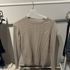 Beige kabelstickad tröja från Bondelid - Säljer en beige kabelstickad tröja från Bondelid. Tröjan har rund halsringning och långa ärmar. Klassisk och stilren design med ribbade muddar vid ärmslut och nederkant. Perfekt för lager-på-lager under kyligare dagar. Storlek M