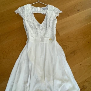 Vit spetsklänning med v-ringning - Superfin vit klänning från CHIARA FORTHI (bubbleroom) med spets upptill och v-ringad hals. Klänningen har korta spetsärmar och en lätt utställd kjol i tunt material. Perfekt för studenten.