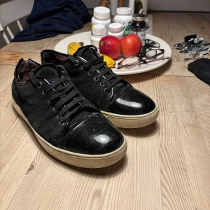 Lanvin skor  - Säljer ett par svarta sneakers från Lanvin med snygga lackdetaljer på tå och häl. Skorna har snörning och vit platt sula. Perfekta för dig som gillar stilrena men ändå unika sneakers. Bästa till priset lite difekter 