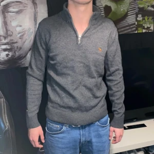 Grå halvzip-tröja från Abercrombie & Fitch - Säljer en stilren grå halvzip-tröja från Abercrombie & Fitch. Tröjan har hög krage med dragkedja och är ribbad vid ärmslut och nederkant. Perfekt för lager-på-lager och passar till det mesta. Han på bilden är 180 cm och väger 62 kg. 