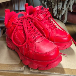 Röda sneakers från Buffalo - Säljer ett par chunky röda Buffalo sneakers med platt sula och rund tå. Skorna har snörning och är tillverkade i syntetmaterial.