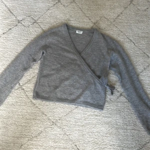 Grå omlottkofta från Kappahl - Säljer en grå omlottkofta från Kappahl med knyt i sidan. Koftan är stickad och har långa ärmar samt v-ringning. Perfekt för lager-på-lager och enkel att matcha med olika outfits.