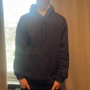 Mörkblå hoodie från Ralph Lauren - Säljer en stilren mörkblå hoodie från Ralph Lauren med broderad logga på bröstet. Tröjan har huva med dragsko och en stor magficka. Perfekt för en avslappnad och snygg look. Storleken är M men den passar S och tröjan är helt oanvänd
