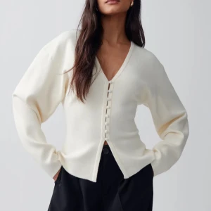  kofta med knappar - Säljer en stilren krämvit kofta med v-ringning och knappar framtill. Tröjan har lång ärm och en något lös passform, perfekt att styla till både jeans och kjol. Superenkel att matcha med andra plagg!