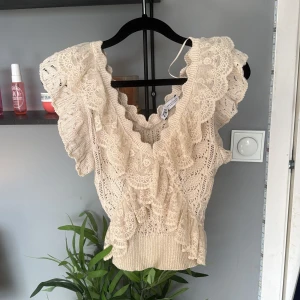 Beige spetsblus med volang från Zara - Säljer en superfin beige spetsblus från Zara med v-ringning och volangdetaljer.💗💗Har inte använt den en typ 2 gånger så den är som ny💗Blusen är ärmlös och har ett romantiskt spetsmönster samt ribbad nederkant. Perfekt för dig som gillar feminina detaljer och unik design.💗💗