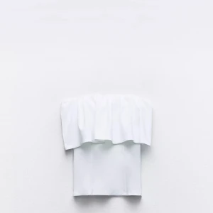 Vit axelbandslös tubtopp med volang - Säljer en stilren vit axelbandslös tubtopp med bred volang upptill. Perfekt för dig som vill ha en enkel men trendig topp till sommaren. Snygg att matcha med både kjol och jeans.