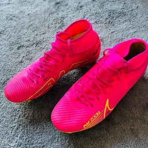 Nike Zoom fotbollsskor i neonrosa och gul - Säljer ett par Nike Zoom fotbollsskor i en riktigt snygg neonrosa färg med gula detaljer och svart Nike-logga. Skorna har snörning, högre skaft och dobbar för bra grepp på planen. Perfekta för dig som vill sticka ut på fotbollsplanen!