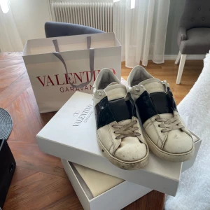 Valentino Open sneakers med svart detalj - Säljer ett par vita Valentino Open sneakers med bred svart läderdetalj över mitten. Kommer med originalkartong och dustbag. Har ej kvitto