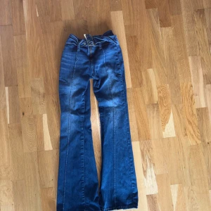 Blå bootcut jeans med hög midja - Säljer ett par blå bootcut jeans med hög midja och klassiska fickor både fram och bak. Jeansen har markerade sömmar längs benen och stängs med dragkedja och knapp. Perfekta för dig som gillar retrostil!