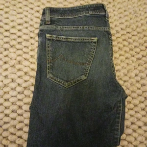 Jacob Cohën - Säljer ett par mörkblå jeans från Jacob Cohën med klassisk femficksdesign och guldfärgad knapp. Jeansen har en rak passform och subtila slitningar framtill. Perfekta för dig som gillar stilrena och tidlösa jeans. Size w31 L31