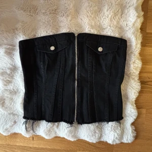 Svart jeanskorsett från Zara - Säljer en korsettopp i jeansmaterial från Zara🖤Toppen har dragkedja framtill, två fickor med knappar och råa kanter nertill. Baksidan har smock för extra stretch och passform. Använd en gång. Storlek L men sitter som en M.
