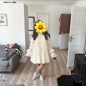 Ljusgul volangklänning från Lis Bonne Atelier - Supersöt ljusgul klänning från Lis Bonnl Atelier i 100% bomull. Klänningen har volanger, långärmade puffärmar och en luftig, lös passform med kort längd. Perfekt för vår och sommar!