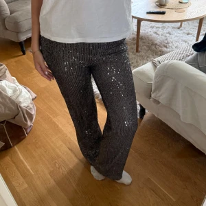 Grå/silver glittriga byxor med paljetter - Säljer ett par svarta byxor med glittriga paljetter. Byxorna har rak passform och normal midja, storlek Xs men passar mig som är 170