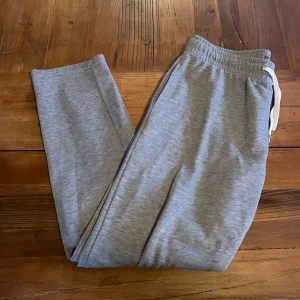 Grå mjukisbyxor från Primark - Säljer ett par klassiska grå mjukisbyxor från Primark med dragsko i midjan och resår. Byxorna har raka ben och en bakficka. Perfekta för chill eller träning.