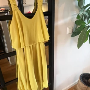 Gul klänning från Love21 - Säljer en solgul klänning från Love21 med breda axelband och lös passform. Klänningen har ett lager på lager-utseende upptill och ett mjukt, fallande tyg som ger en luftig känsla. Perfekt för varma dagar och somriga tillfällen.
