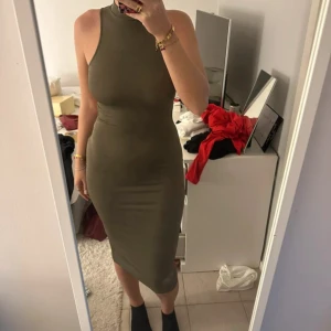 Olivgrön tight klänning med öppen rygg - Säljer en olivgrön tight klänning med hög hals och öppen rygg som knyts baktill. Klänningen är ärmlös och har en kroppsnära passform som slutar strax under knäet. Perfekt för dig som vill ha en stilren och trendig look.
