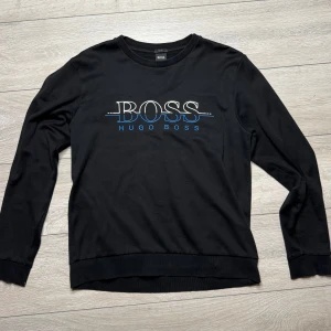 Svart sweatshirt från Hugo Boss - Hugo Boss svart tröja med blå och vit text I gott skick, 7/10 Som ses på bilderna har plagget små hål (som inte syns vid användning) och en reva på den nedre delen av ryggen som är lagad. Storlek: Slim fit L (mellan M och L) För mer information är du välkommen att skriva till oss privat!