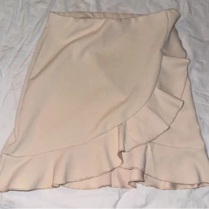 Beige omlottkjol med volang från NLY ONE - Supersöt beige omlottkjol från NLY ONE med volangdetaljer längs nederkanten. Storlek S