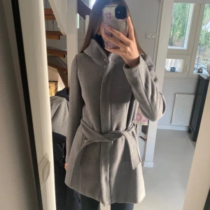 Grå kappa med bälte och huva - Grey spring/autumn coat with a hood and a string to adjust the waist size. Size is Xs/32. In very good condition and like new. 