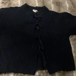 Mörkblå kofta med knyt från Gina Tricot - Säljer en mörkblå kofta från Gina Tricot med knyt framtill. Koftan är croppad och har lång ärm. Perfekt att slänga över en topp för en snygg lager-på-lager-look.