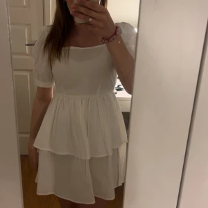 Vit kortklänning med puffärmar och volang - Supersöt vit klänning med puffärmar från boohoo, aldrig använd med prislapp kvar. Fyrkantig ringning och volang i midjan. Klänningen har en kort längd och knytning i ryggen för extra detalj.
