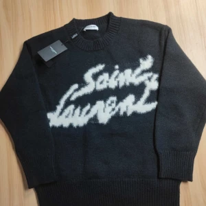 Svart stickad tröja från Saint Laurent - Säljer en svart stickad tröja från Saint Laurent med vit logotyp framtill. Tröjan har rund halsringning och långa ärmar med ribbade muddar. Perfekt för dig som gillar exklusiva och stilrena plagg. Tröjan har en normal passform och är väldigt skön. Vid fler funderingar är det bara att skriva.