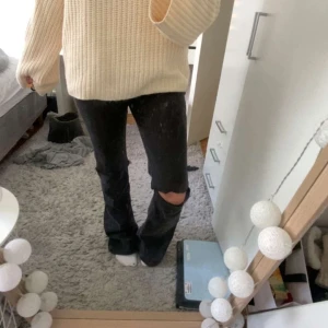 Svarta bootcut jeans med hål på knät - Säljer ett par svarta bootcut jeans med stort hål på båda knäna. Byxorna har en klassisk femficksmodell och är i en lite lösare passform nertill. Perfekta för en avslappnad och trendig look.