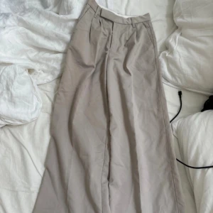 Beige kostymbyxor med vida ben - Snygga beige kostymbyxor med medium midja och vida ben. Byxorna har pressveck, hällor för bälte och stängs med dragkedja och hake fram. Perfekta för en stilren look. Storlek EUR 30 och ifrån H&M 💕