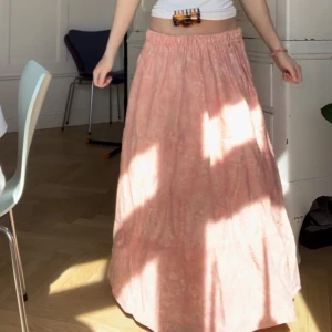 Ljusrosa långkjol med mönster - Säljer en ljusrosa långkjol med vitt mönster och resår i midjan. Kjolen har en luftig och flowy passform, perfekt för sommaren. Jag är typ 164 och den passar bra i längden🥰