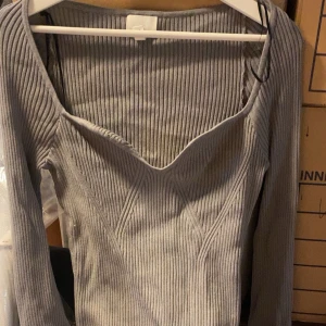 Grå ribbad långärmad topp - Snygg grå ribbad topp med lång ärm och v-ringad hals. Figurnära passform och stretchigt material som sitter skönt på kroppen. Perfekt att styla med jeans eller kjol.